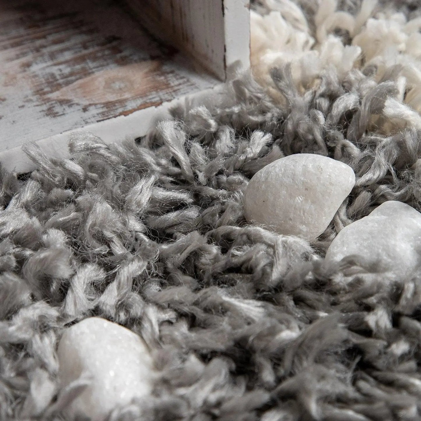 Close-up of a textured gray rug with white stones on a wooden floor.