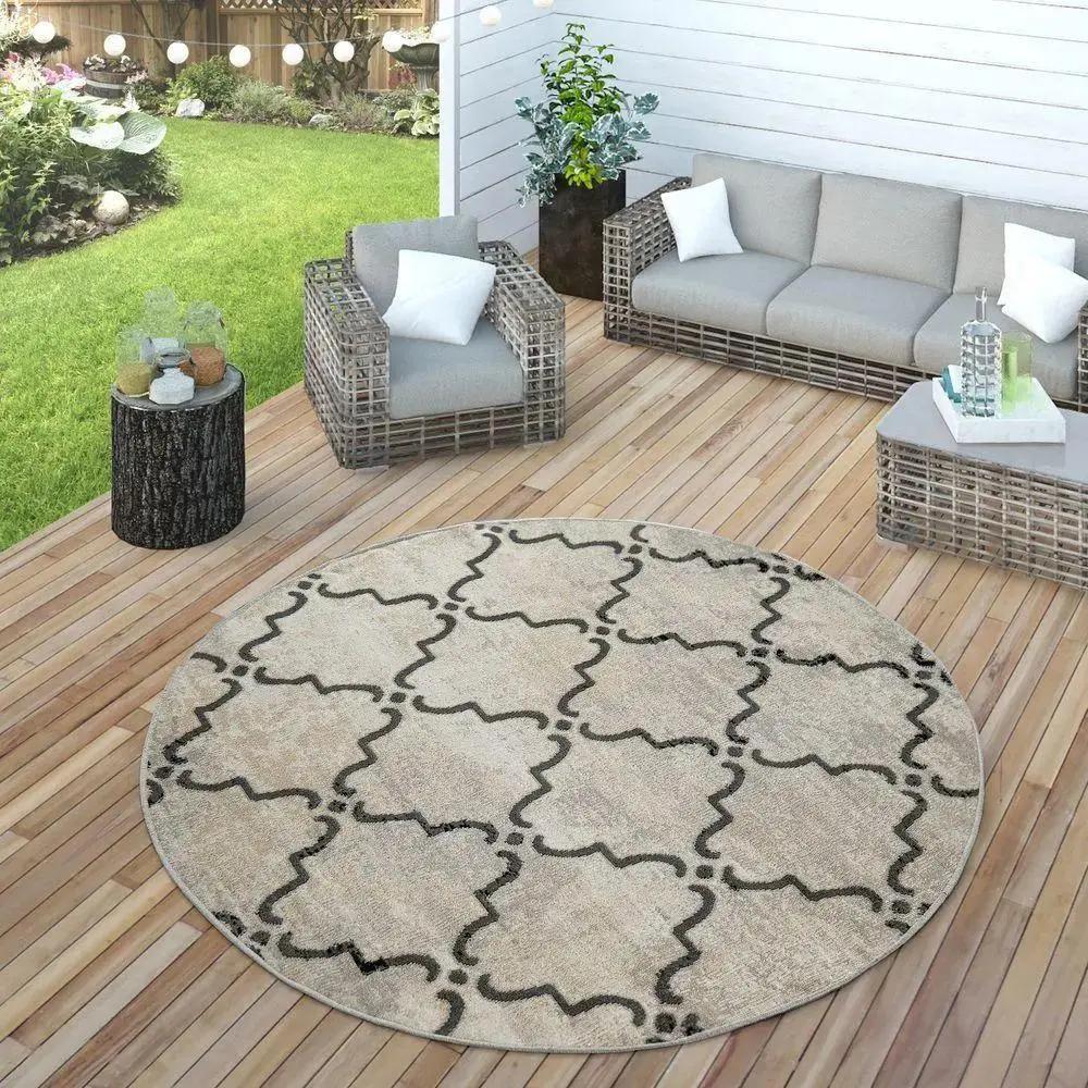 Round outdoor rug with geometric pattern on a wooden deck, surrounded by patio furniture.