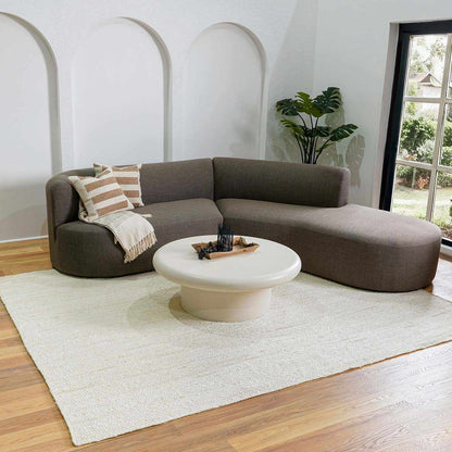Brown sectional sofa with a white coffee table in a room with a large window.