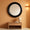 Round black-framed mirror on an orange wall with a wooden side table and lamp below.