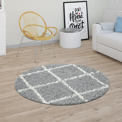 Round gray area rug with white geometric pattern on a wooden floor, with a chair, table, and sofa in the background.