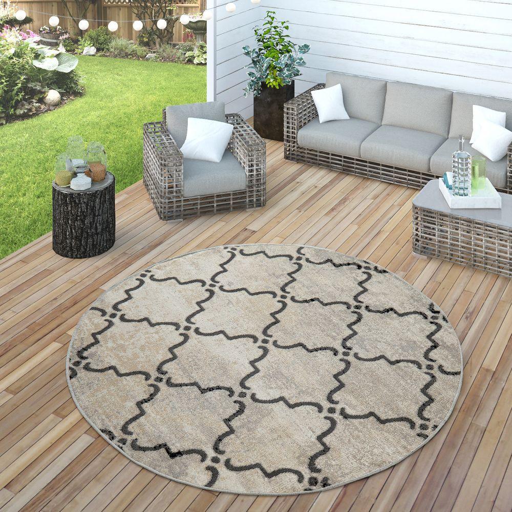 Round outdoor rug with geometric pattern on a wooden deck, surrounded by patio furniture.