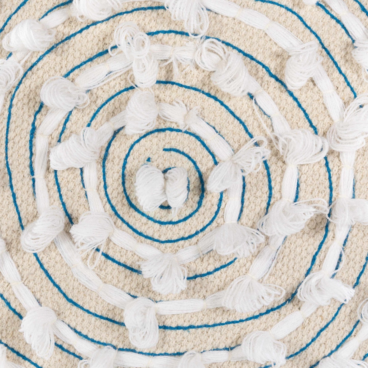 Close-up of a textured round rug with concentric circles and tassels.