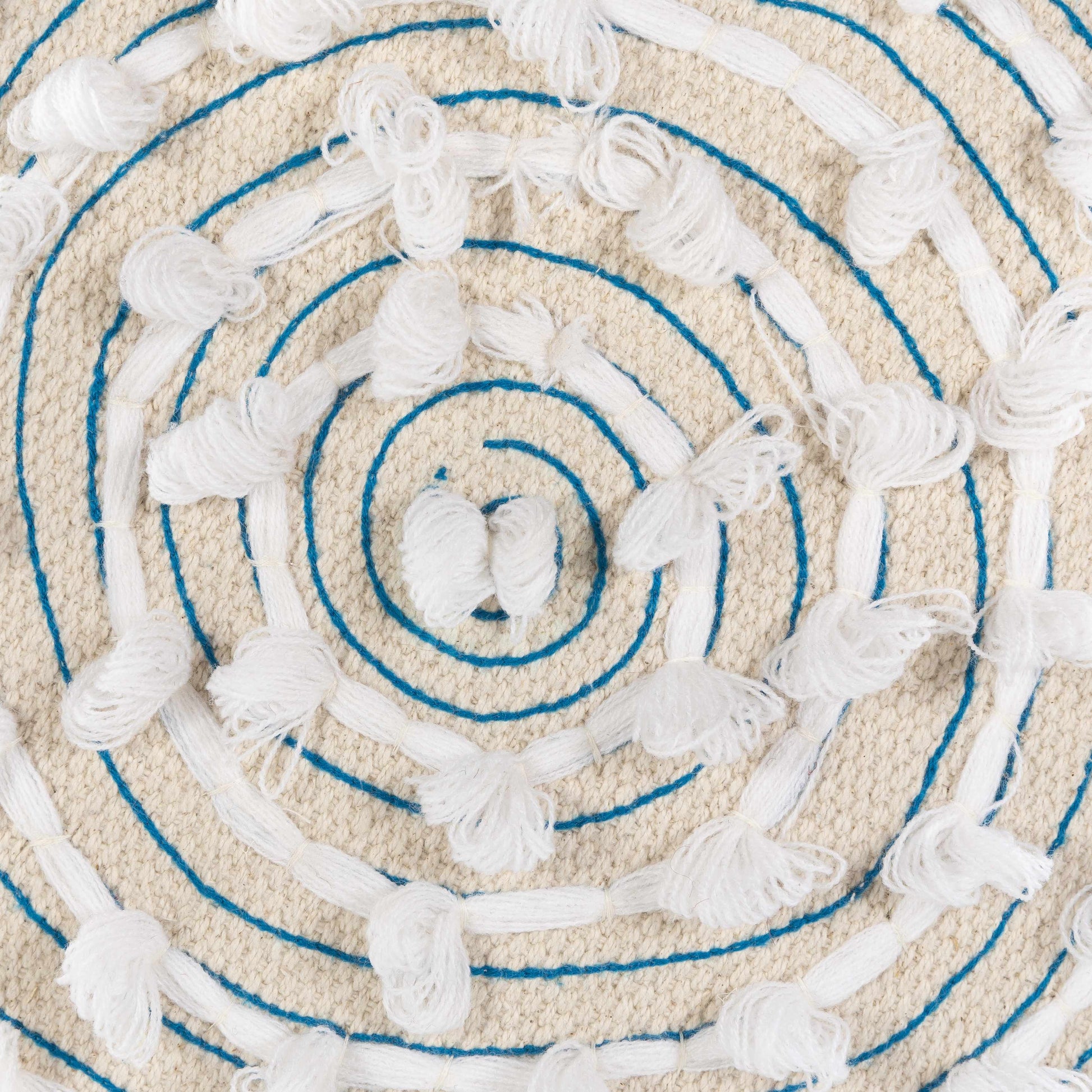 Close-up of a textured round rug with concentric circles and tassels.