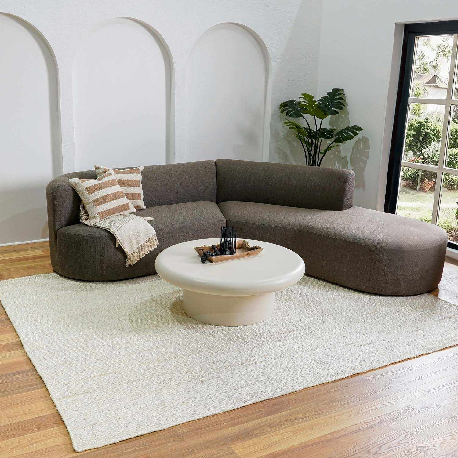 Brown sectional sofa with a white coffee table in a room with a large window.