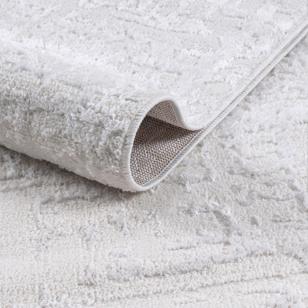 Close-up of a textured white rug with a folded corner on a matching background.