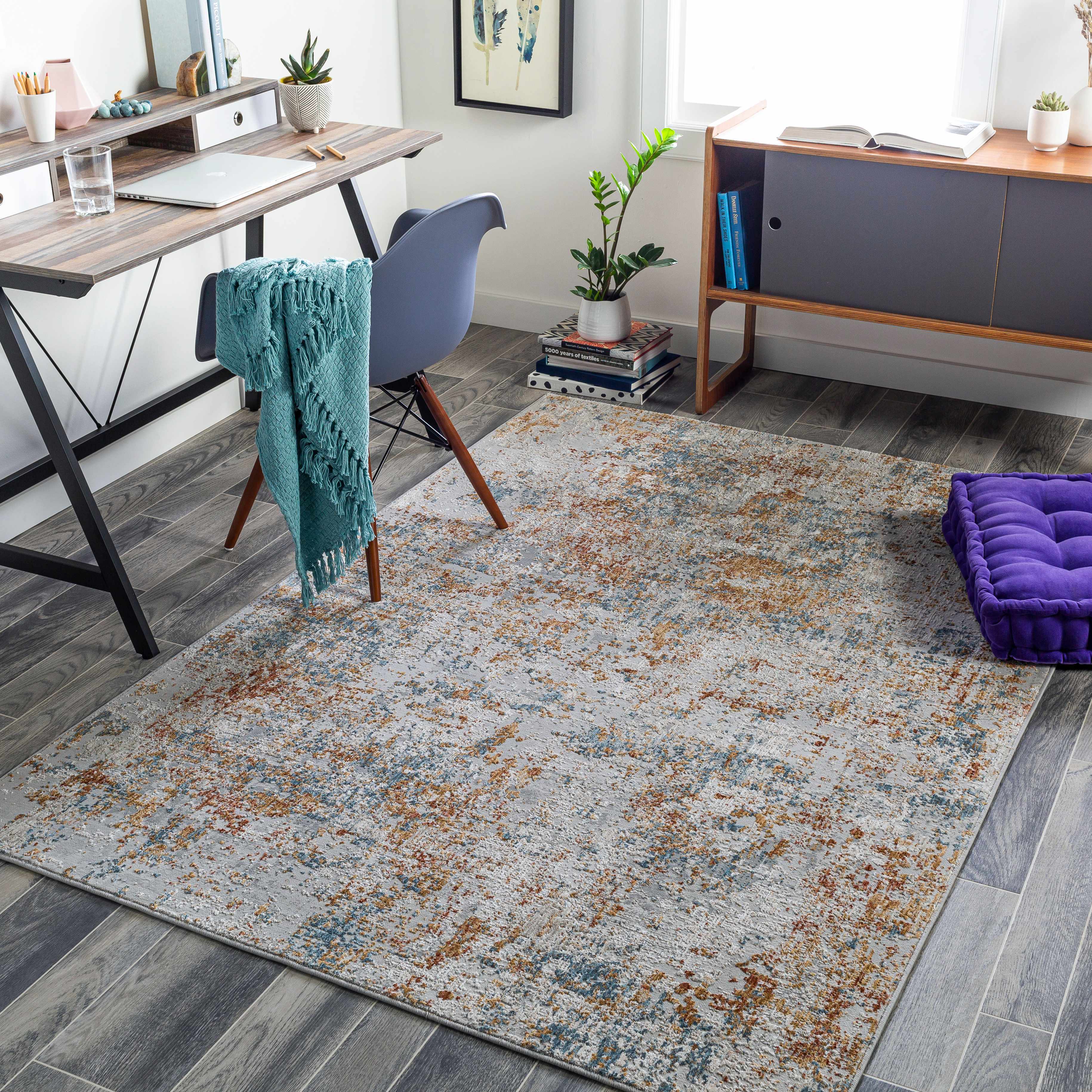 Living room with a patterned rug, purple cushion, and a desk with a laptop.