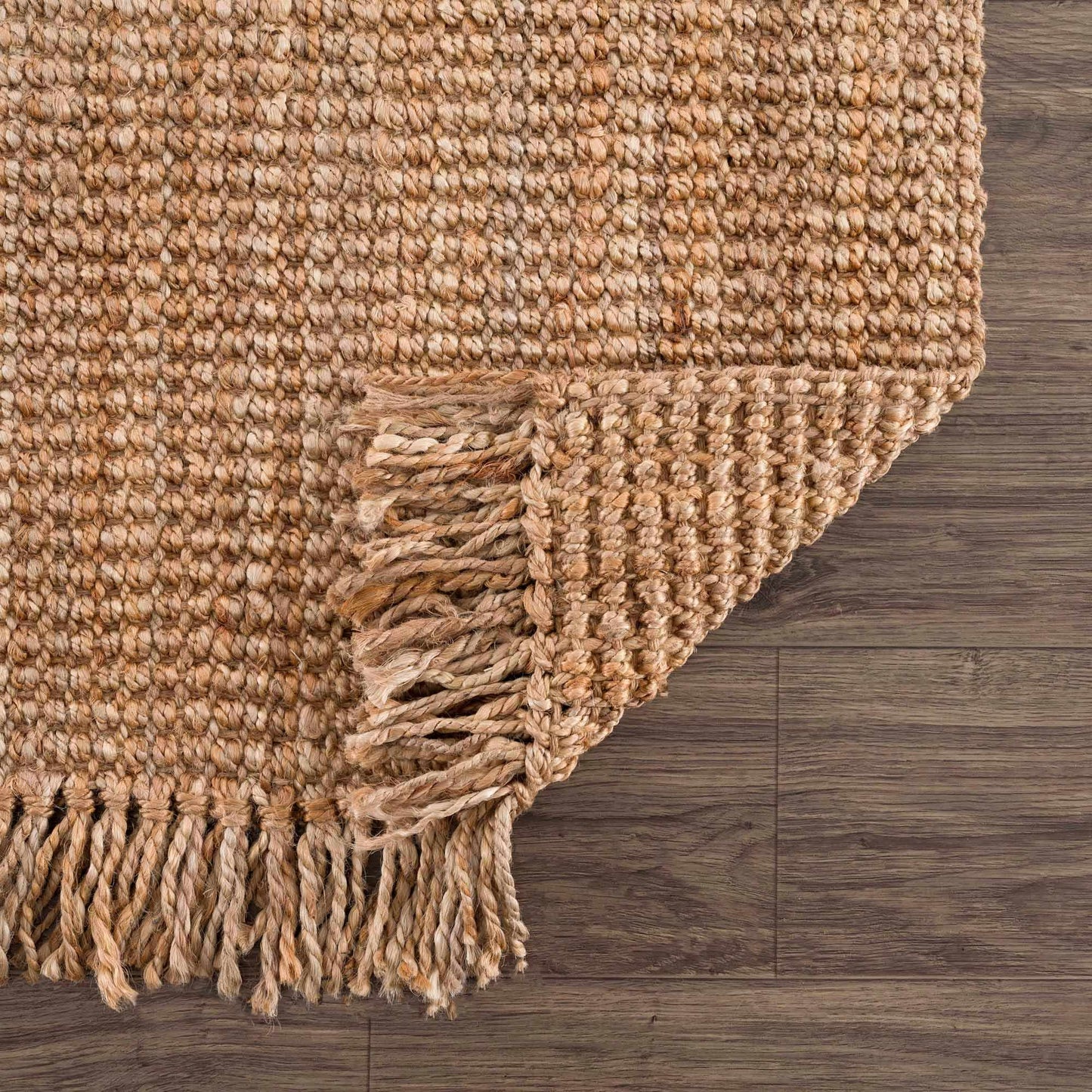 Close-up of a textured beige rug with fringes on a wooden floor.