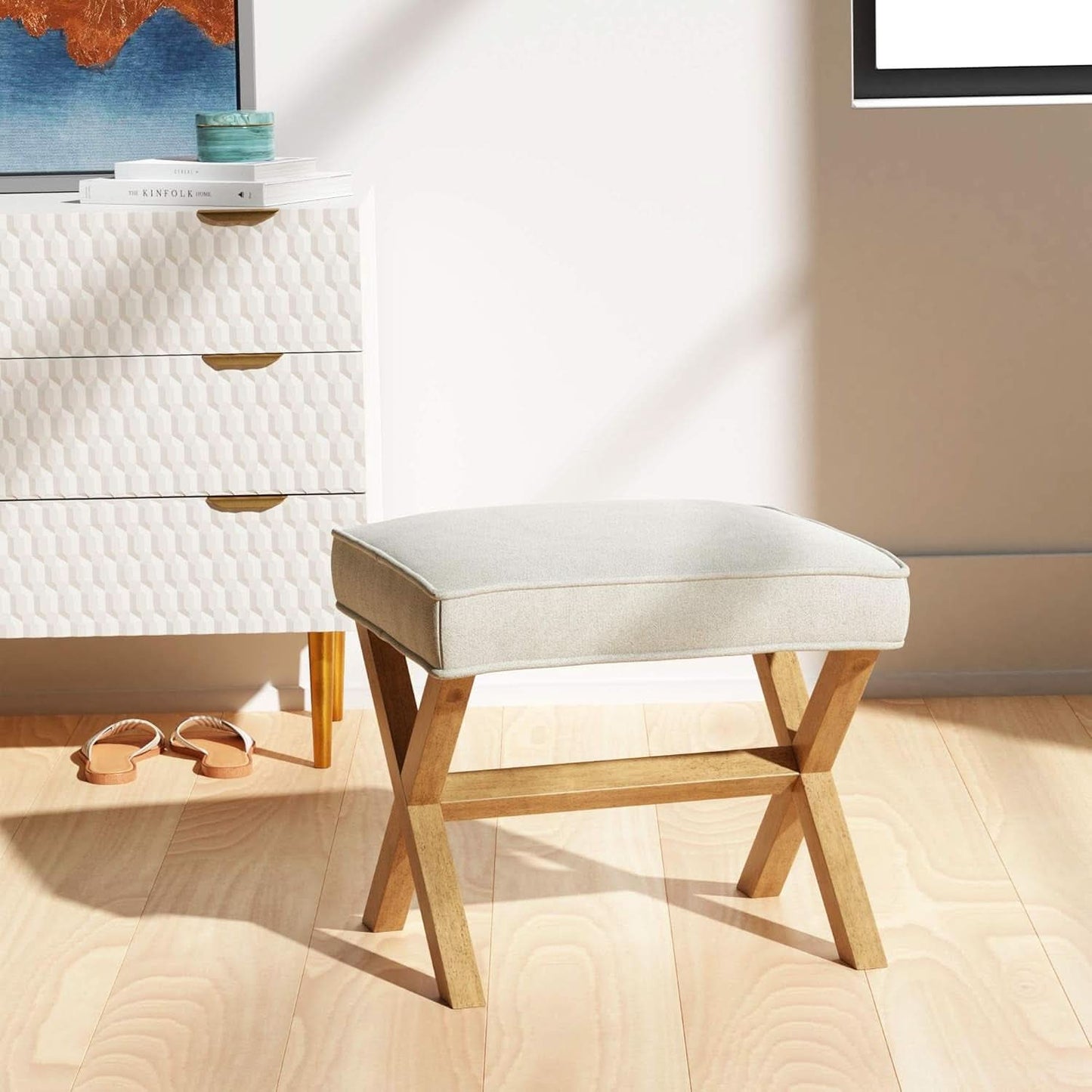 Light gray cushioned stool with wooden legs in a room setting.