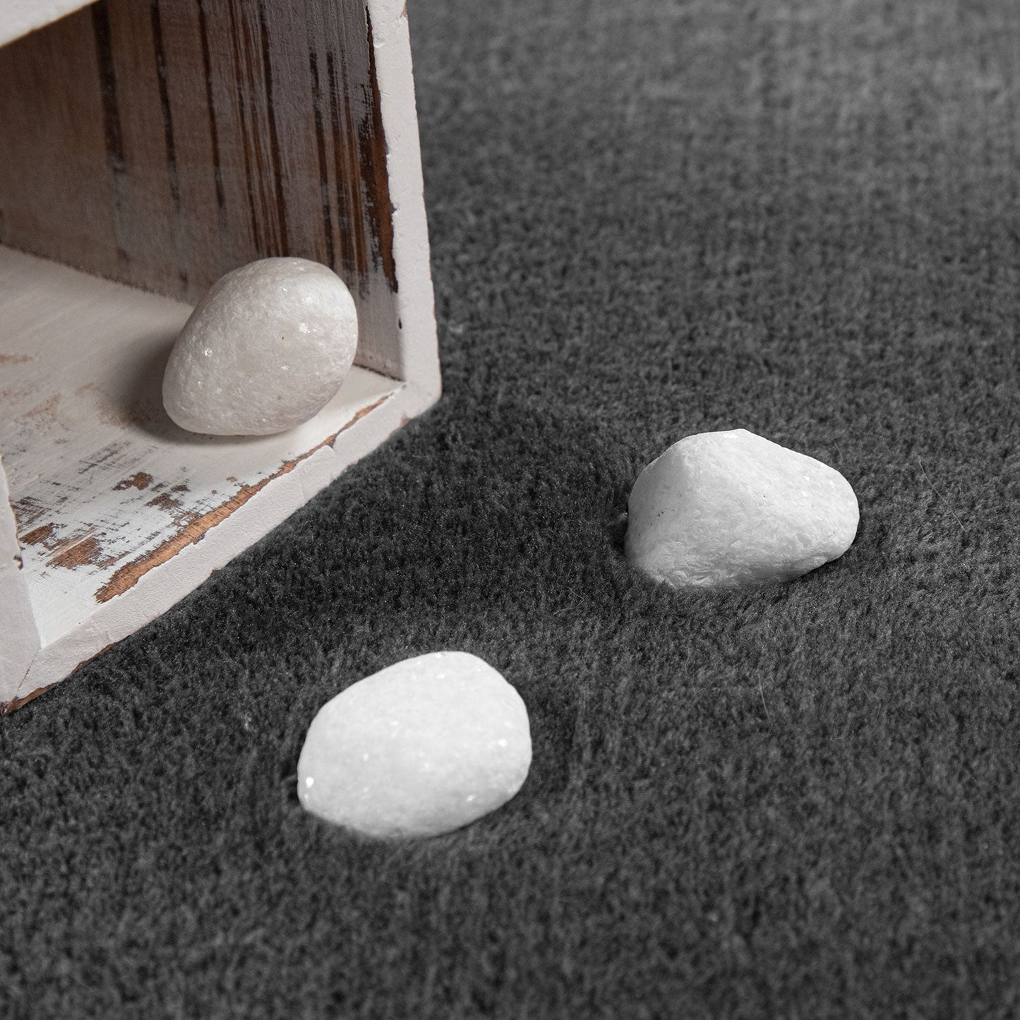 Three white stones on a textured gray surface with a wooden box in the corner.