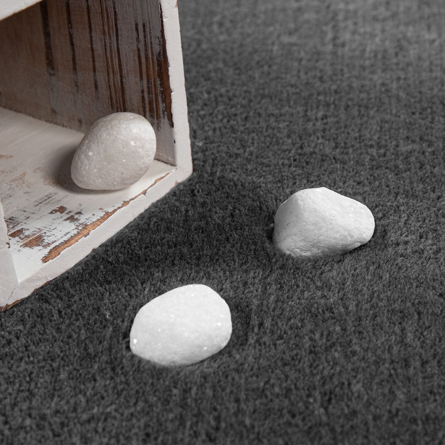 Three white stones on a textured gray surface with a wooden box in the corner.