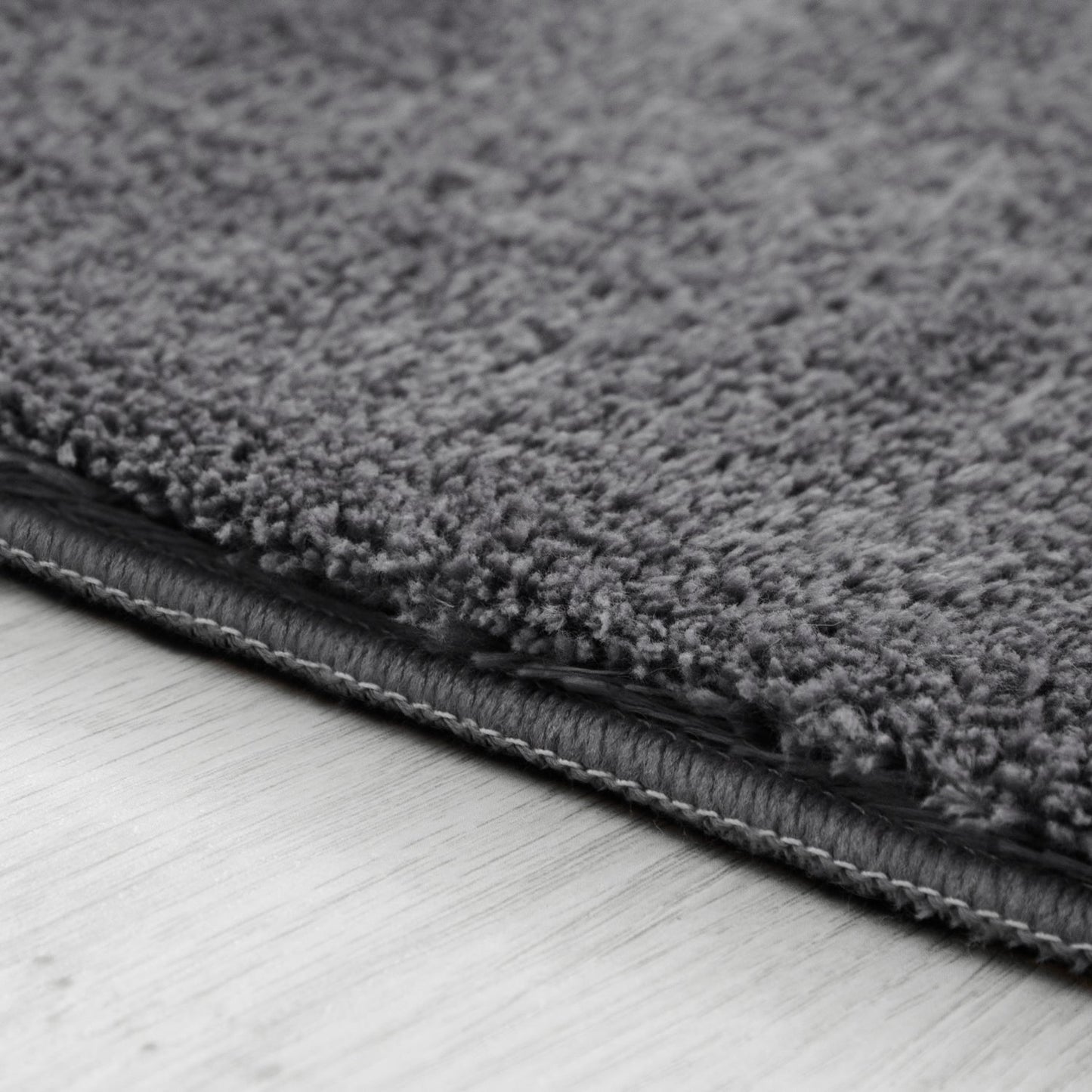 Close-up of a gray textured rug on a light wooden floor.