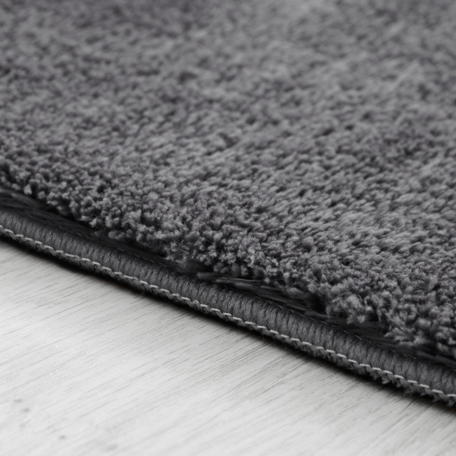 Close-up of a gray textured rug on a light wooden floor.