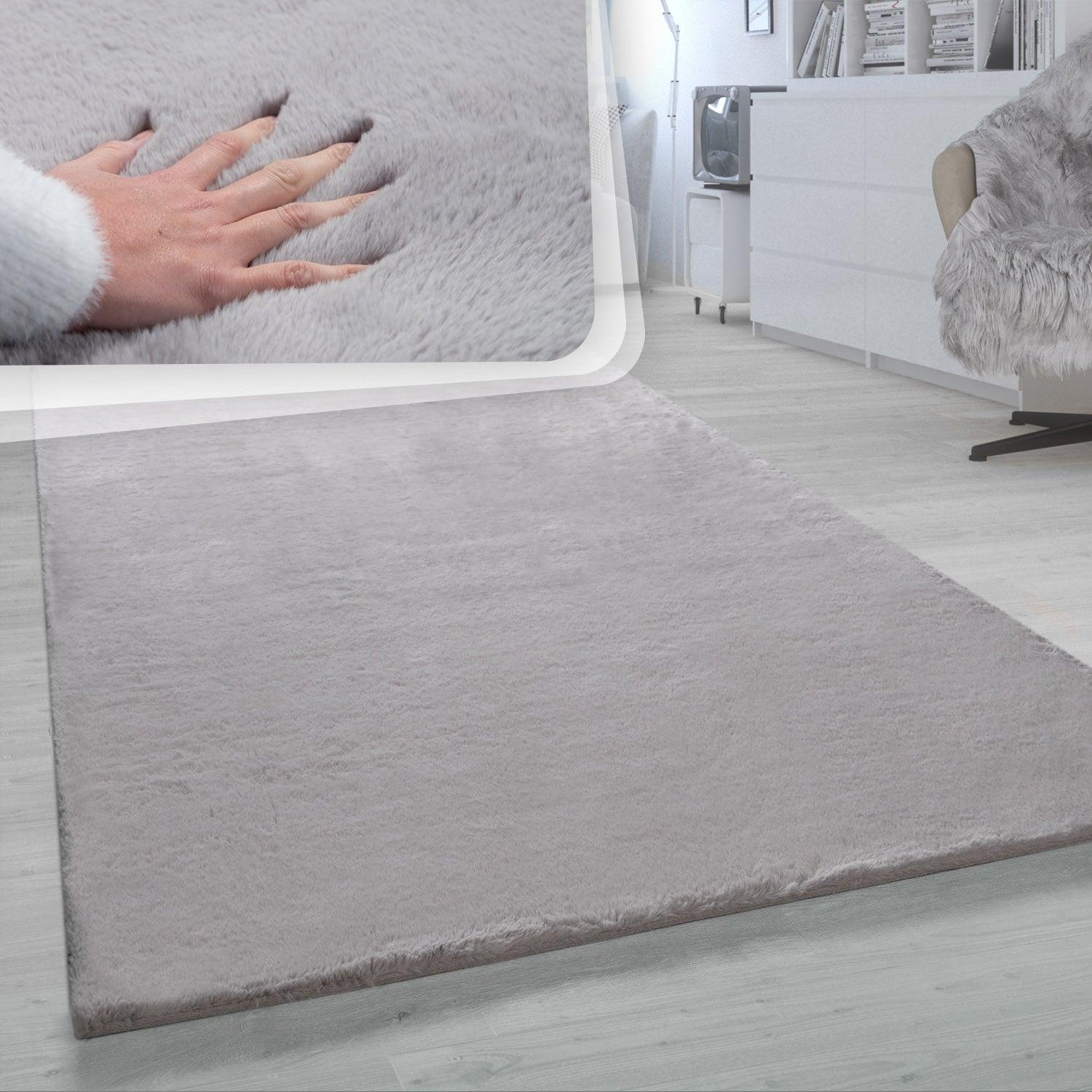 Gray rug on a light wooden floor with a hand touching the rug's texture.