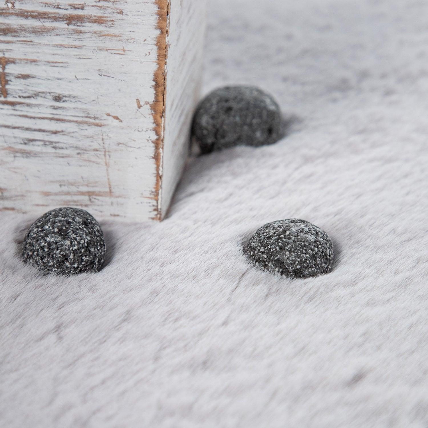 Three textured stones on a sandy surface with a wooden box in the background