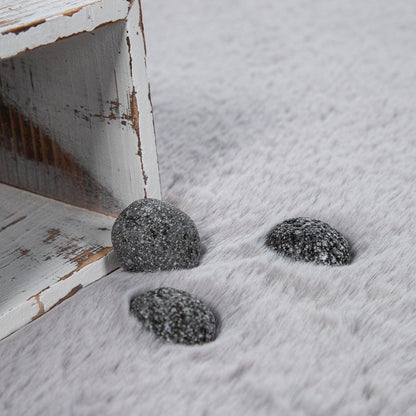 Three dark stones on a snowy surface next to a rustic wooden bench.