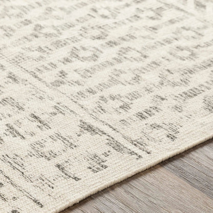 Close-up of a textured area rug with a distressed, abstract pattern in cream and gray, shown on a light wood floor.